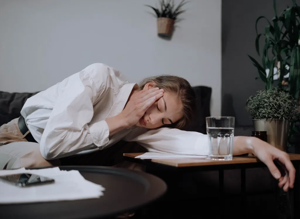Woman resting her head on her arm at a side table, eyes closed and one hand pressed to her face